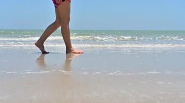 Sahil sörfünde yalın ayak yürüyen gezgin kadın. Kapalı kumsalda yürüyen kadın bacakları ve ayakları.