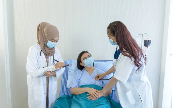 Muslim female doctor giving advice discussion and young Asian female doctor using stethoscope checking pressure to elderly patient sitting in bed at hospital. Medicine and health care concept.