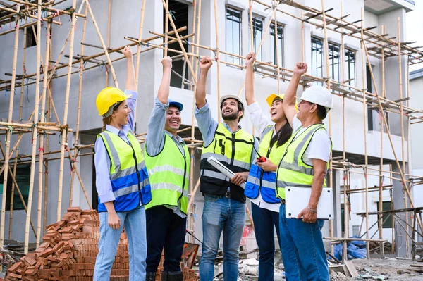 Group of contractors, engineers and formats in safety vests with helmets hands up to work together to successfully complete a construction project on construction site. cooperation and success concept