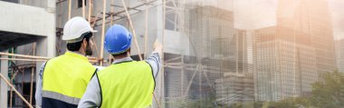 Banner of Construction engineer and architect check plan working with the blueprint on construction site. They are in safety vests with helmets for safety. Back view of the Construction project concept. 