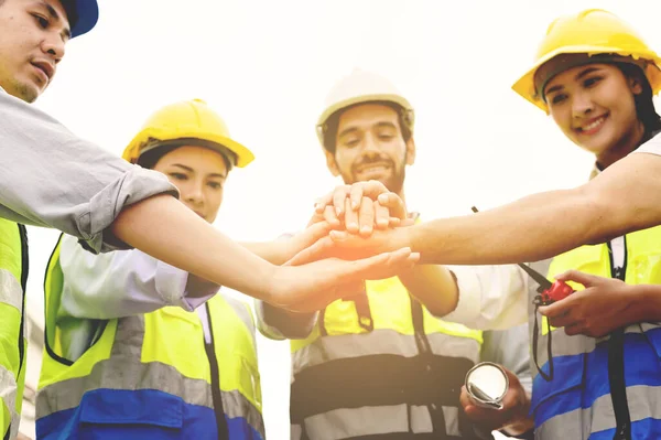 Group of contractors, engineers and formats in safety vests with helmets join hands to work together to successfully complete a construction project on construction site. cooperation and success concept