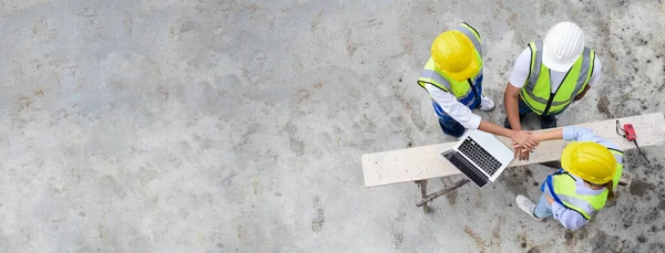 Top view of contractors, engineers and formats team in safety vests with helmets working with laptops, standing on under-construction building site. Banner cover design. Home building project.