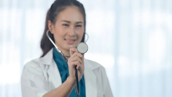 Young female medical doctor holding stethoscope head with blurred muslim doctor checking elderly patient on the background. Select focus to stethoscope head. Medicine and health care safe concept