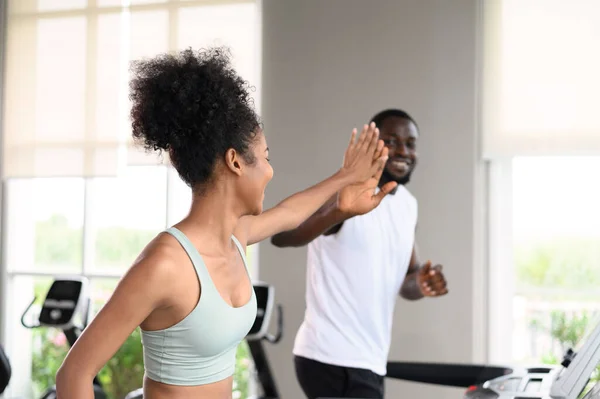 Black African American couple clapping hands together while running on the treadmill at fitness club. Healthy lifestyle, training in gym. Fitness partners give a high five. healthy concept