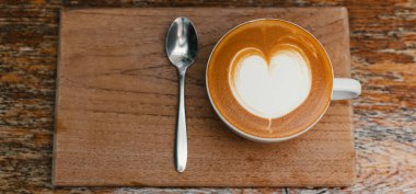 Tahta tepside kahve kaşığıyla beyaz bardakta sıcak kahvenin en üst görüntüsü. Boşluğu kopyala