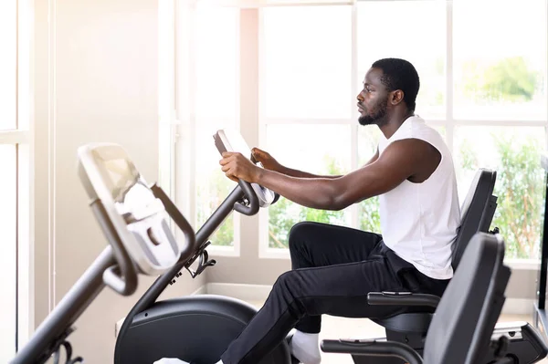 Side view of African American man exercising on the exercise bike in indoor fitness club. Healthy and Fitness concept