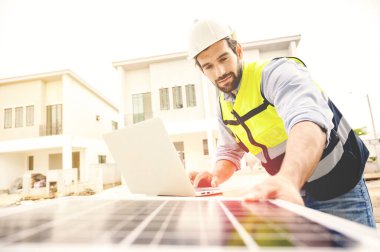 Kasklı, çelik yelekli elektrikçi güneş pili tesisini kontrol etmek için laptop kullanıyor. Yeşil enerji elektriği. Sürdürülebilir kaynaklar kavramı