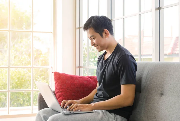 Young asian businessman wear casual clothing relax sitting and working with laptop computer on cozy couch in living room at home.. WFH. work from home concept