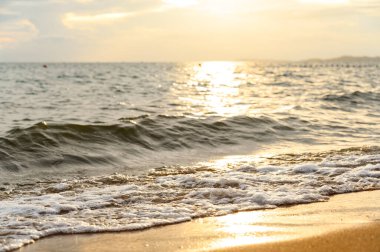 Deniz suyu yumuşak dalgası yaz aylarında gün batımında kumlu sahil kıyısına çarpıyor. yaz tatili etkinliği arka plan kavramı.