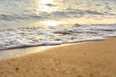 Deniz suyu yumuşak dalgası yaz aylarında gün batımında kumlu sahil kıyısına çarpıyor. yaz tatili etkinliği arka plan kavramı.