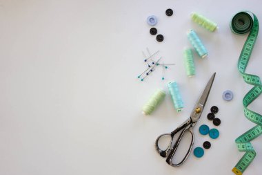 Dikiş aksesuarlarıyla donatılmış. Makas, mezura, iğne, iplik, beyaz arka plandaki düğmeler. Aksesuarlar dikiliyor