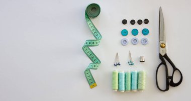 Dikiş aksesuarlarıyla donatılmış. Makas, mezura, iğne, iplik, beyaz arka plandaki düğmeler. Aksesuarlar dikiliyor