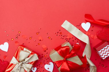 Preparation and celebration of Valentine's Day. Creative composition with gifts, ribbons and hearts on a red background. Copy space.