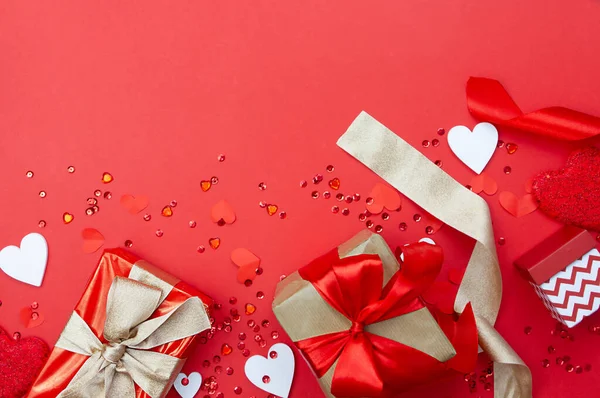 Preparation and celebration of Valentine's Day. Creative composition with gifts, ribbons and hearts on a red background. Copy space.