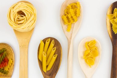 Different types of pasta in wooden spoons close up on a white background.