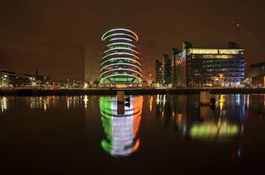 Dublin, İrlanda - 13 Kasım 2021: İrlanda bayrağını taklit eden ve suya yansıyan halka kirişli Dublin Kongre Merkezi 'nin güzel geniş açılı akşam manzarası. Modern Dublin mimarisi