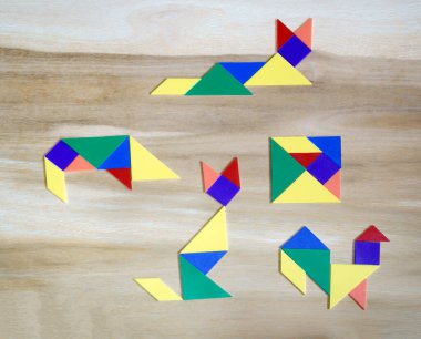 Tahta bir arka planda yedi düz poligondan oluşan tangram bulmacaları. Orijinal kare ve dört hayvan.