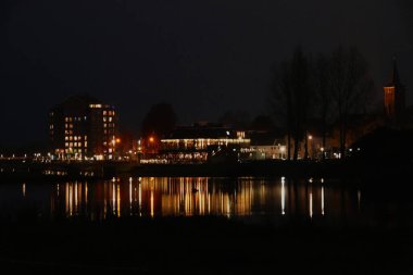 Geceleri Hollanda 'nın Hardenberg kasabasının ufuk çizgisi. Şehir ışıkları Vecht nehrine yansıyor..