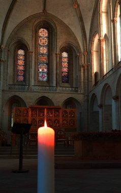 Kilisenin içi: yanan bir mum, sunak ve arka planda vitray pencereler.. 