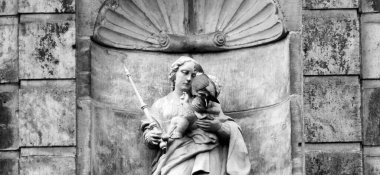 A common wood pigeon sitting on a statue. It's a statue of Maria above the entrance of an old monastery from the 14th century