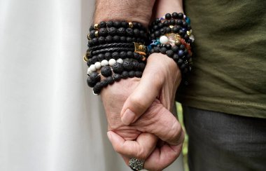 Kıdemli erkek ve kadın el ele tutuşuyor. Lav taşı ve diğer tahta bilezikler takıyorlar..