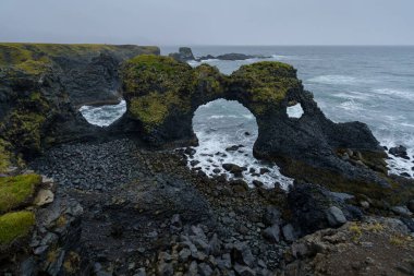 İzlanda doğa manzarası. Gatklettur - Arnarstapi köyü yakınlarındaki Snaefellsnes yarımadasında Arch Rock, bazalt kaya uçurumu. Yağmurlu havada fırtınalı dalgalar