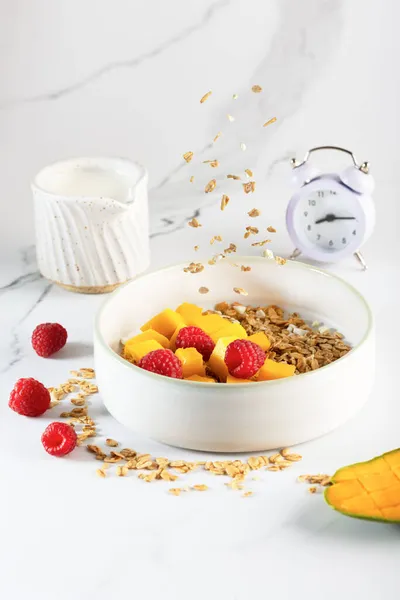 Bowl of granola with yogurt, milk and fresh raspberries, blueberries, mango for a healthy breakfast on a white marble table — Stock Photo, Image