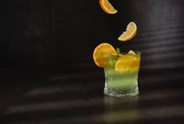 Limonatalı bardaklar ya da limonlu, portakallı ve naneli mojito kokteyli koyu arkaplanda soğuk, ferahlatıcı bir içecek..
