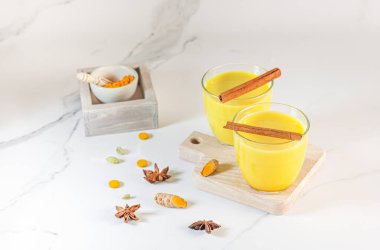 Üzerinde zerdeçal tozu, taze zerdeçal kökü, anason ve tarçın olan el yapımı altın bir süt. Baharat ve bitki kavramı. Arka planda Ayurvedic içki. Metin için boşluk. 