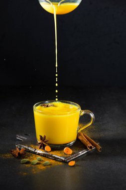 İçinde zerdeçal tozu, taze zerdeçal kökü, anason ve siyah üzerine tarçın olan el yapımı altın bir süt. Baharat ve bitki kavramı. Arka planda Ayurvedic içki. Metin için boşluk. 