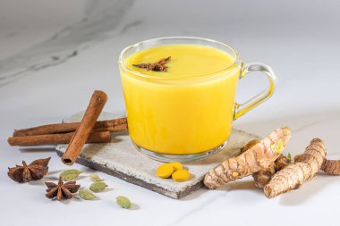İçinde zerdeçal tozu, taze zerdeçal kökü, anason ve tarçın olan bir bardak altın süt. Baharat ve bitki kavramı. Arka planda Ayurvedic içki. Metin için boşluk. 