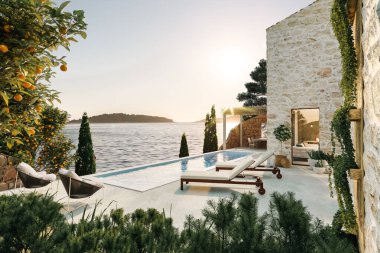 Üç boyutlu taş ev, gün boyunca teras ve yüzme havuzuyla denizin üzerindeki kayanın üzerinde duruyordu.