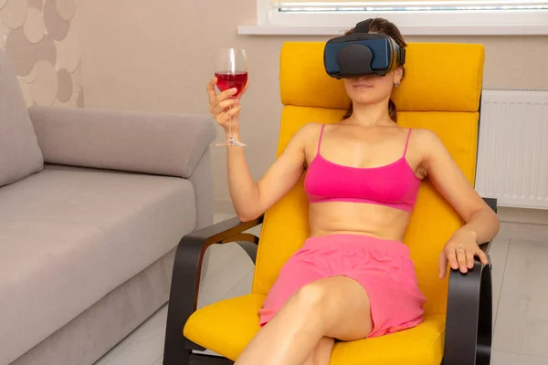 Woman at home in armchair with glass of wine and virtual glasses relaxes