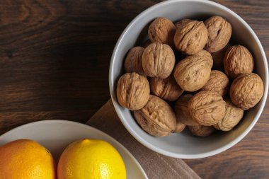 Limonlar, portakallar ve cevizler ahşap bir masada gri bir kasede