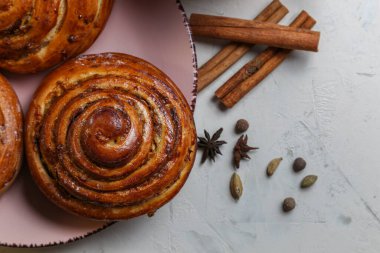 Bir fincan süt ve baharatla parlak bir masada pembe bir tabakta tarçın ruloları.