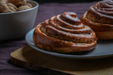 Tarçınlı çörekler gri bir tabakta, karanlık bir masada, cevizli.