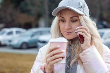 Çekici genç bir kadın telefonda konuşuyor ve elinde tek kullanımlık bir bardak içki bardağıyla yakından çekilmiş bir portre, seçici bir odaklanma.