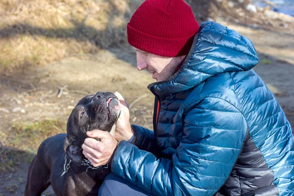 Close-up portrait of a man and a dog, a black pit bull faithfully looks into the eyes of his owner, love for animals