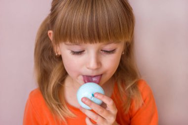 Güzel küçük kız elinde mavi bir tatlı makaronu tutuyor. Yakın plan, tatlı pastalar. Çocukluk duyguları, seçici odaklanma.