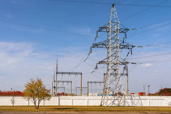 Support columns for high-voltage wires behind fence and barbed wire. At power plant. Autumn season, yellow foliage on trees