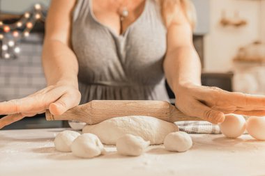 Ayrıca büyük göğüslü ve gri dekolteli bir model Noel arifesinde ya da aile tatili arifesinde mutfakta ahşap tahta kesme iğnesiyle hamuru yuvarlıyor.