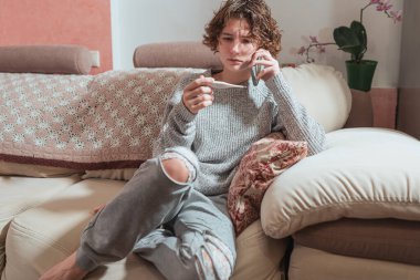Hasta ya da üşümüş, okula ya da üniversiteye gitmeyen. Termometresi olan hasta bir genç kız evde kanepe otururken akıllı telefon doktoruyla konuşuyor. Kıvırcık kahverengi saçlı sağlıksız genç kız üşütmüş ve cep telefonuyla konuşuyor.. 