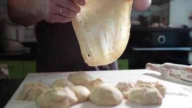 Ellerinle pizza hamuru fırlatıyorsun. Önlüklü erkek fırıncı ev mutfağında dururken ince rulo pizza hamuru fırlatıyor. Ev yemeği, evde pizza pişirmek.