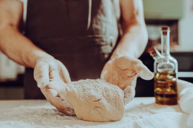 Erkek fırıncının elleri yoğurulmuş hamur ile yakın plan un serpiştiriyor. El yapımı hamur fırını