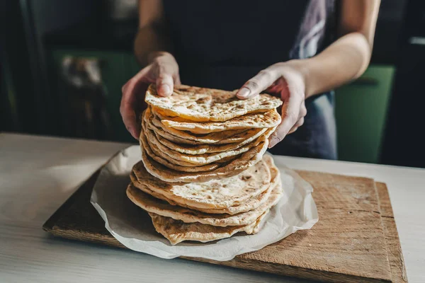 Thin round cakes of lavash are stacked, hands of cook stretch lavash forward for testing. Spanish flatbread or armenian lavash close-up