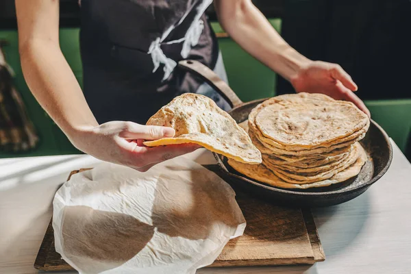 面包师的手正在从一个铸铁煎锅里取出平塔面包 私人小面包店生产工艺面包和皮塔面包 厨房的围裙烘培师把现成的比萨面包堆在一起 — 图库照片