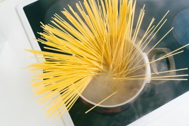 Tenceredeki spagetti, elektrikli seramik hob 'da kaynar suda pişirilir. Üst manzara, yumuşak odak, sarı glütensiz mısır makarnası bolonez. Kaynar suda spagetti.