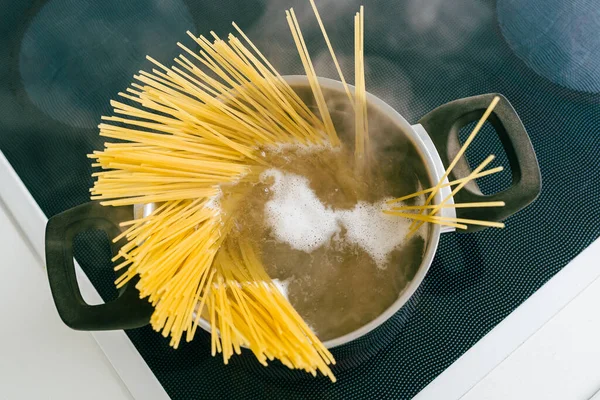 Tenceredeki spagetti, elektrikli seramik hob 'da kaynar suda pişirilir. Üst manzara, yumuşak odak, sarı glütensiz mısır makarnası bolonez. Kaynar suda spagetti.