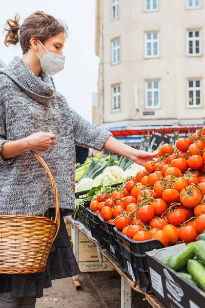 Buying fresh bio vegetables at the grocery market. girl with wicker basket for groceries chooses ripe tomatoes on counter of grocery market