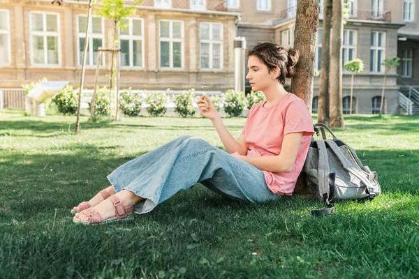 attractive teenage girl sits in park on lawn, holds small chamomile flower in hands, thoughtful emotion on face, thoughts of happiness. Positive emotions, mental and emotional health. Listen to silence, enjoy nature